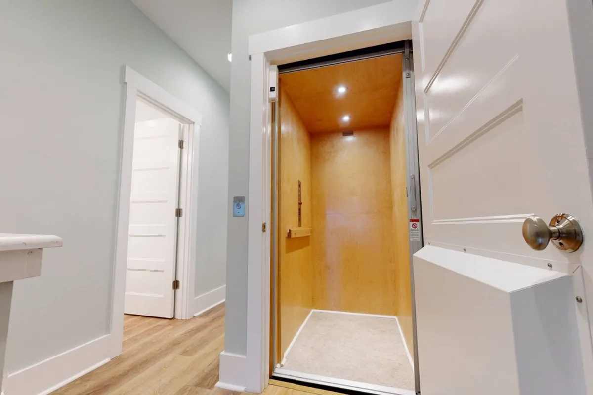 A modern interior view focuses on a private residential elevator with wooden flooring and a nearby doorway. The setting is bright and accessible, clearly showcasing the elevator as an integral part of the home’s layout.