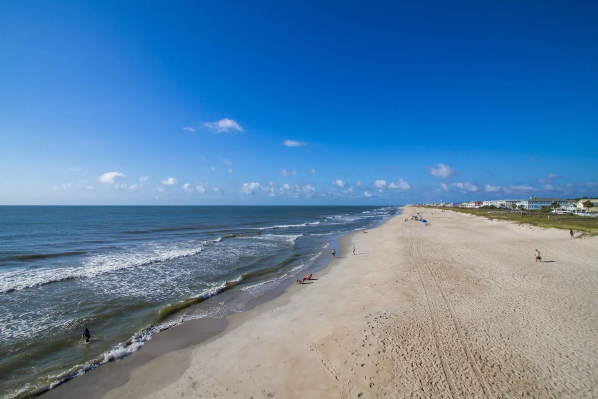 A joyful scene featuring soft sandy beach, gentle ocean waves, and families and individuals enjoying sunbathing, swimming, and walking along the shore under a sunny sky. The atmosphere is lively and inviting, highlighting an inclusive, multi-generational enjoyment of the beach.
