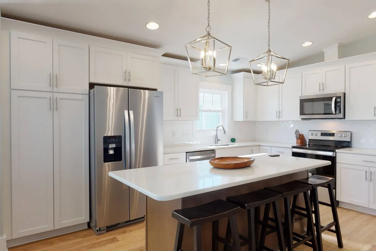 A modern kitchen featuring a large island countertop, stylish pendant lighting, stainless steel appliances, and crisp white cabinetry. The layout is ideal for cooking, entertaining, and hosting celebratory meals.