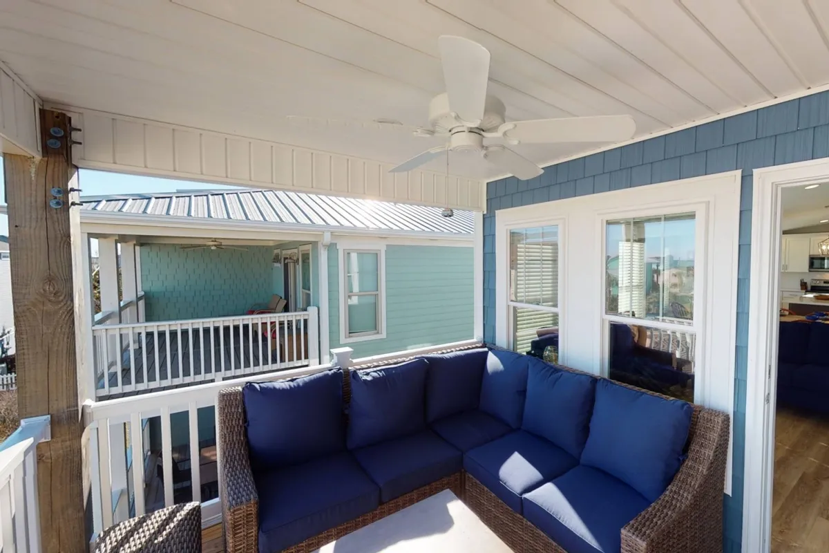 A comfortable outdoor seating area featuring a ceiling fan and stylish blue wall, designed for relaxation and socializing. The space suggests a welcoming environment for enjoying ocean breezes, gathering with friends or family, or unwinding after a beach day.