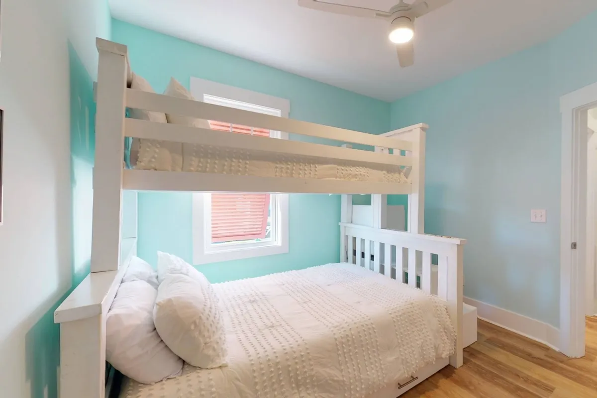 A playful bunk room with a bunk bed, a large window providing ample daylight, and a colorful wall. The setting is cheerful, perfect for children or groups seeking a fun sleepover environment.